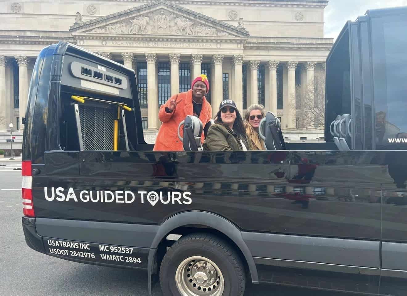 Smiling guests ride in a black USA Guided Tours open-top convertible vehicle outside the National Archives building in Washington, DC